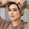 A woman is adjusting an elegant anti-slip inner hijab cap on her head, wearing a brown long-sleeved top.