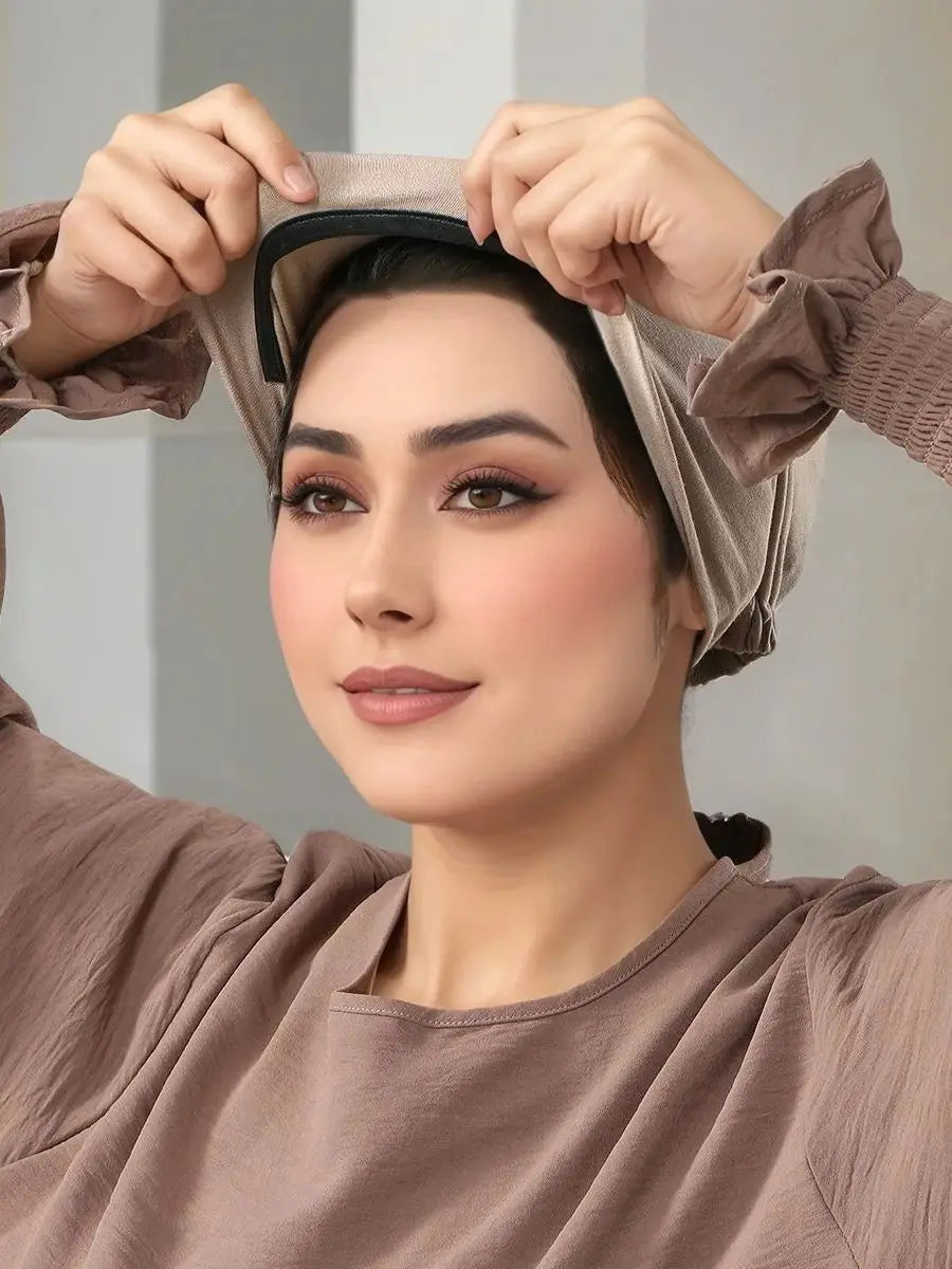 A woman is adjusting an elegant anti-slip inner hijab cap on her head, wearing a brown long-sleeved top.