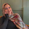 Eine Frau trägt einen modischen Schleier mit aquarelliertem Blumenmuster als Hijab und blickt in die Kamera.