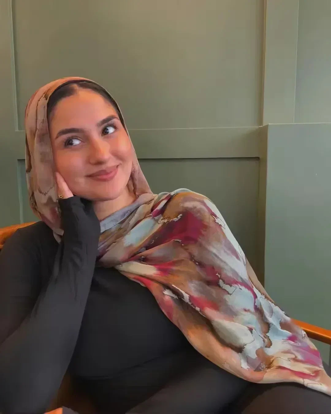Eine Frau trägt einen modischen Schleier mit aquarelliertem Blumenmuster als Hijab und blickt in die Kamera.