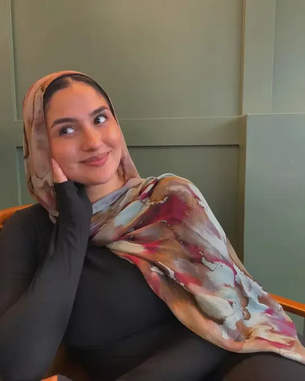 A woman wearing a watercolour floral printed modal shawl hijab scarf is looking towards the camera.