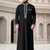 Jubba thobe casual robe for men, embroidered in black with silver detailing, standing in a grand architectural setting.