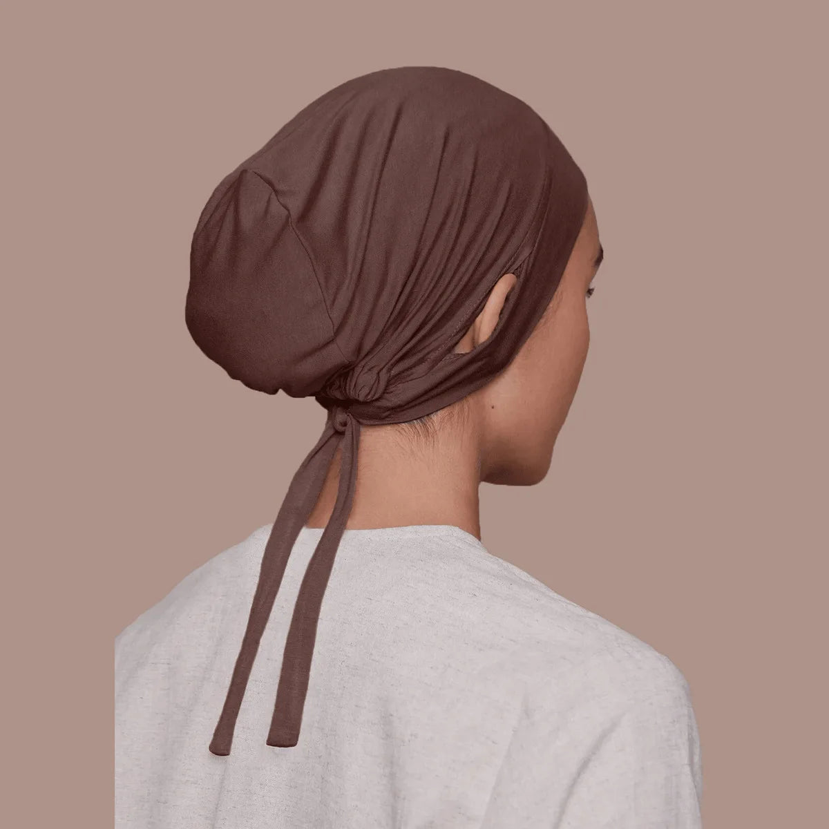 Une femme portant un bonnet inner hijab en cordon marron et un haut gris clair, vue de profil.