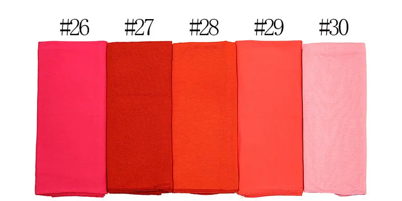 Una fila de cinco pañuelos de hijab doblados para mujeres en tonos rosa, rojo y coral.