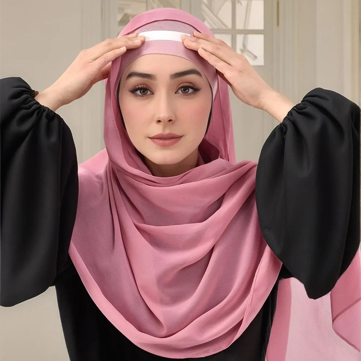 Una mujer con un hiyab rosa está usando una cinta corporal invisible para asegurar su pañuelo y vestido.