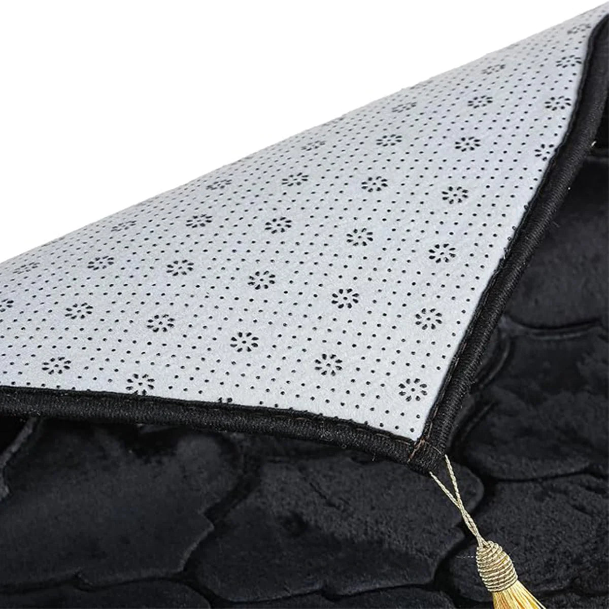 Gros plan d'un tapis de prière noir embossé avec une couverture pointillée blanche et un détail de pompon doré.