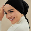 Eine Frau mit schwarzem Hijab und weißem Rollkragenpullover lächelt und richtet ihr Haar.