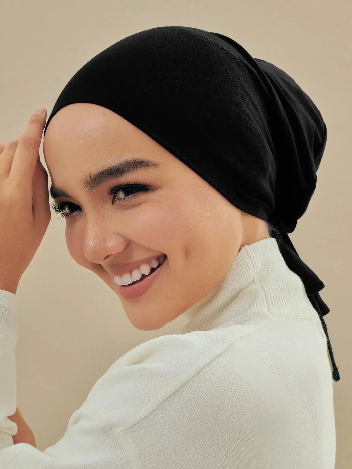 Eine Frau mit schwarzem Hijab und weißem Rollkragenpullover lächelt und richtet ihr Haar.