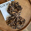 Écharpe pashmina imprimée léopard marron et noir pliée sur une carte blanche, posée sur un tapis tissé.