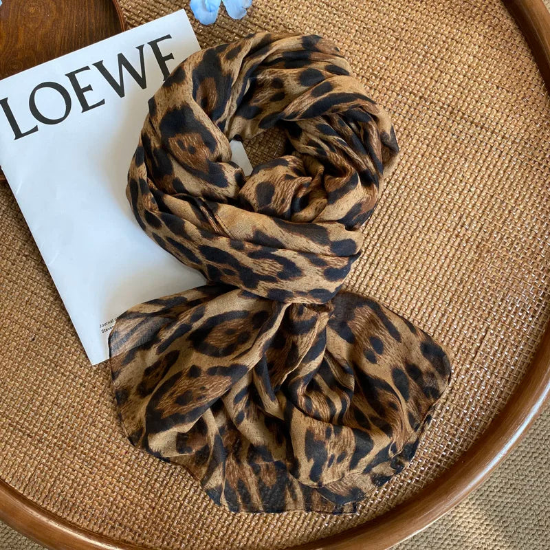 Écharpe pashmina imprimée léopard marron et noir pliée sur une carte blanche, posée sur un tapis tissé.
