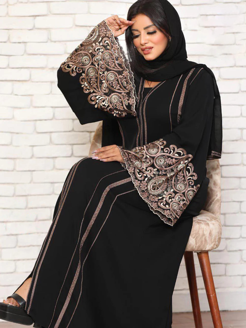 Una mujer vistiendo un elegante abaya largo de manga larga negra con bordados intrincados y un hijab negro.