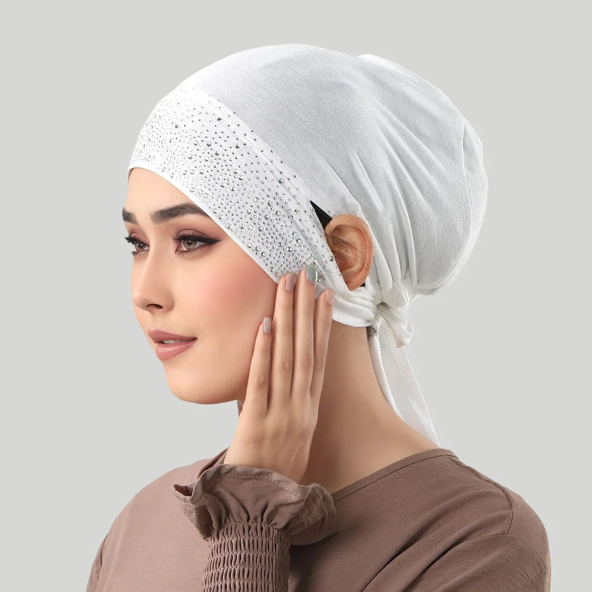 Eine Frau trägt eine weiße Jersey-Baumwoll-Hijab-Mütze mit Punkten und berührt ihr Gesicht.