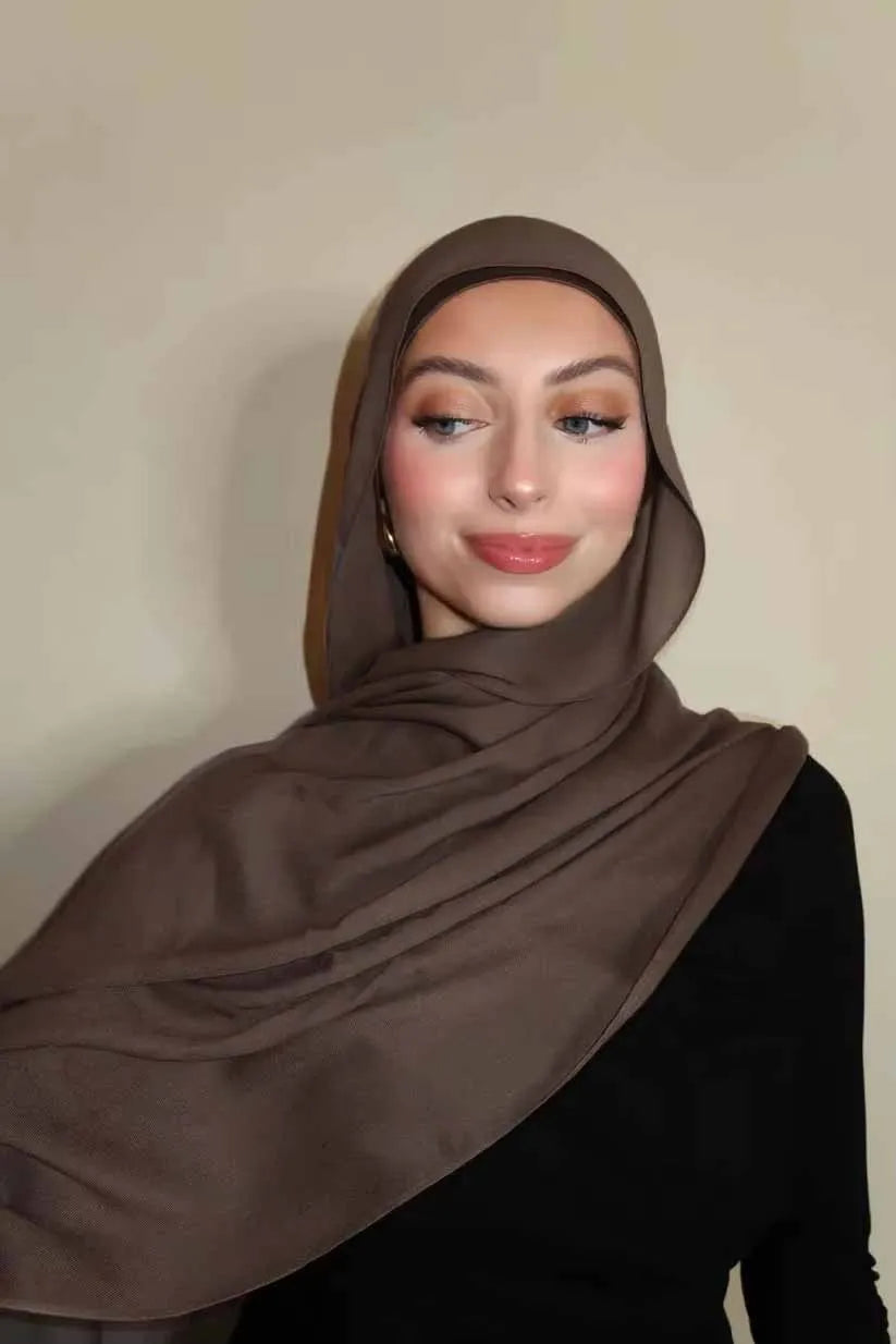 Eine Frau trägt einen solid braunen Gradient-Rayon-Hijab und schwarze Kleidung.