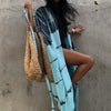 Eine Frau in einem blau-schwarz gemusterten Kimono-Überkleid und einer Strohtasche steht vor einer strukturierten Wand.