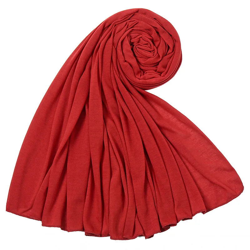 Un foulard hijab en jersey de coton rouge profond roulé et drapé, montrant sa texture douce.
