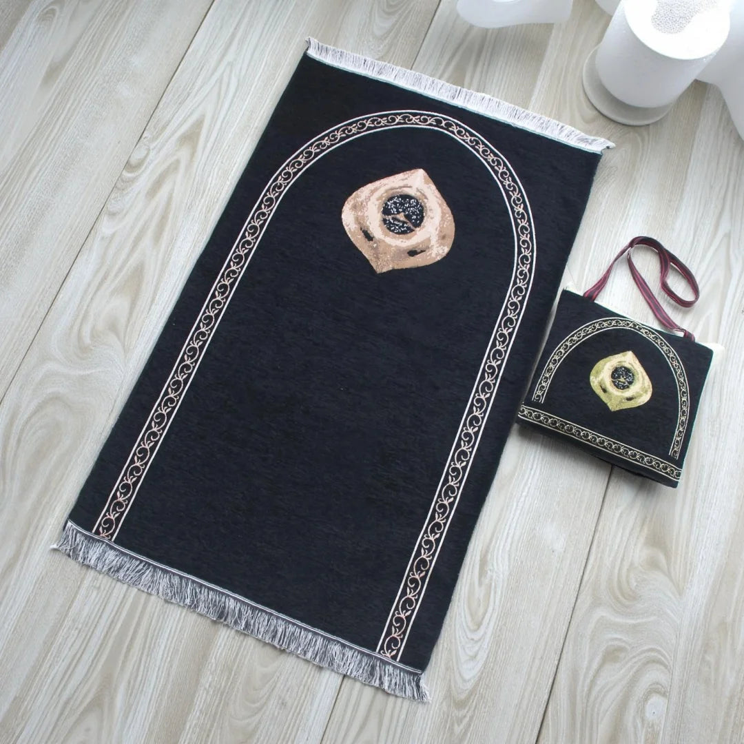 Eine schwarze Gebetsmatte mit bogenförmigem Design und einer goldfarbenen Gebetsperle darauf.