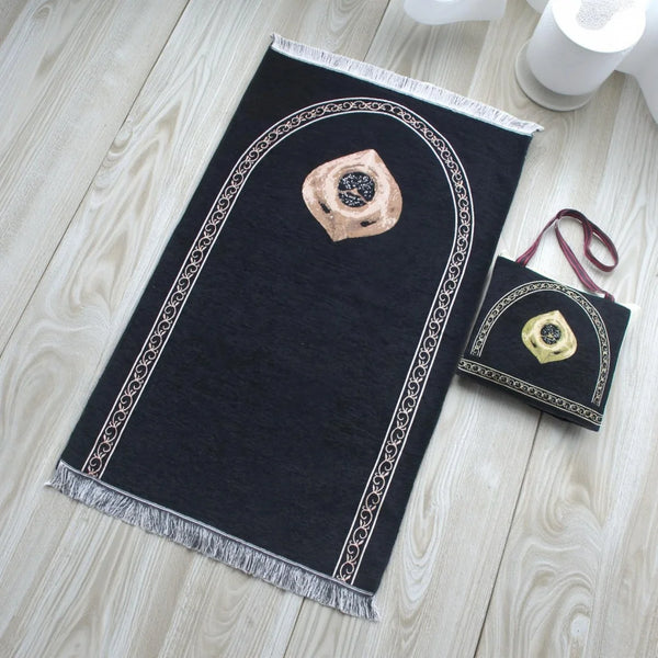 A black prayer mat with an arched design and a gold-colored decorative element is displayed on a light wooden surface.