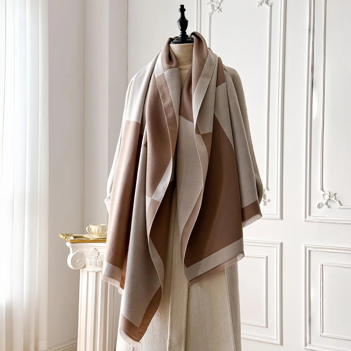 Una pashmina beige con patrones geométricos marrón y crema, drapeada sobre un maniquí.