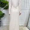 Elegantes, beiges Maxikleid mit hohem Kragen und langen Ärmeln vor einer weißen Wand.
