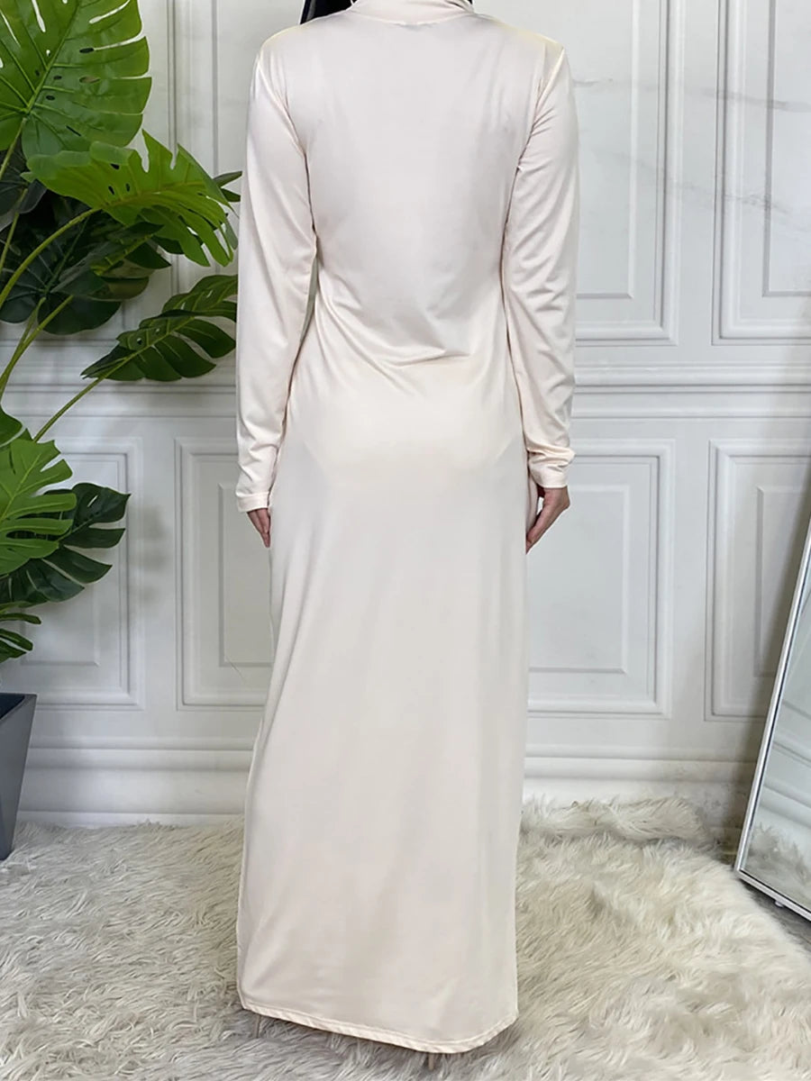 Elegantes, beiges Maxikleid mit hohem Kragen und langen Ärmeln vor einer weißen Wand.