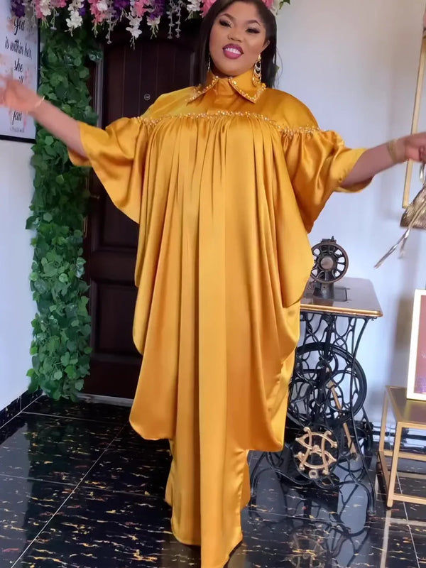 A woman wearing a flowing golden yellow kaftan abaya for evening wear standing in a room.