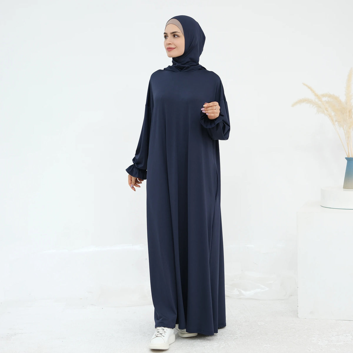 Una mujer vistiendo un vestido abaya suelto y fluido de color azul marino para la oración.
