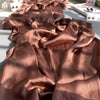 Ein drapiertes Stück aus roségoldenem gekräuseltem Satin-Chiffon in weichen Falten auf einer hellen Oberfläche.