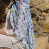 Une femme portant un hijab bleu clair à motifs floraux, assise devant un mur de pierre texturé.