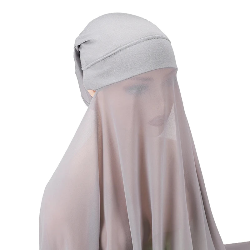 Un conjunto de hijab y chal de gasa instantánea gris claro exhibido contra un fondo blanco.