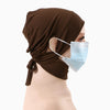 Eine Frau trägt eine braune Jersey-Baumwoll-Hijab-Kappe und eine hellblaue medizinische Gesichtsmaske.