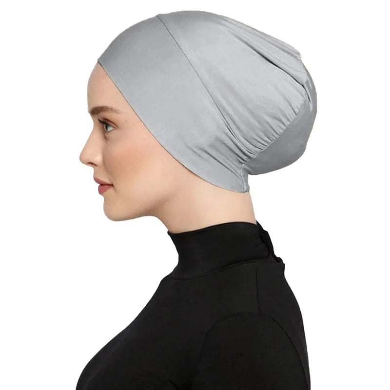 Una mujer vistiendo un turbante instantáneo gris claro en la cabeza, vista de perfil contra un fondo blanco.