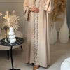 Eine Frau in einem eleganten beige Abaya mit dezentem Blattstickerei steht in einem hellen Innenraum.