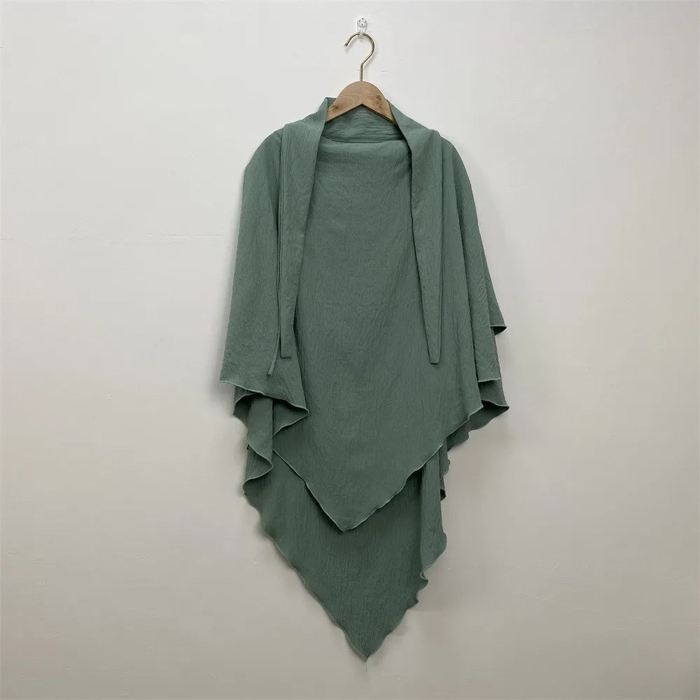 A teal two-layer everyday hijab scarf draped on a wooden hanger against a white wall.