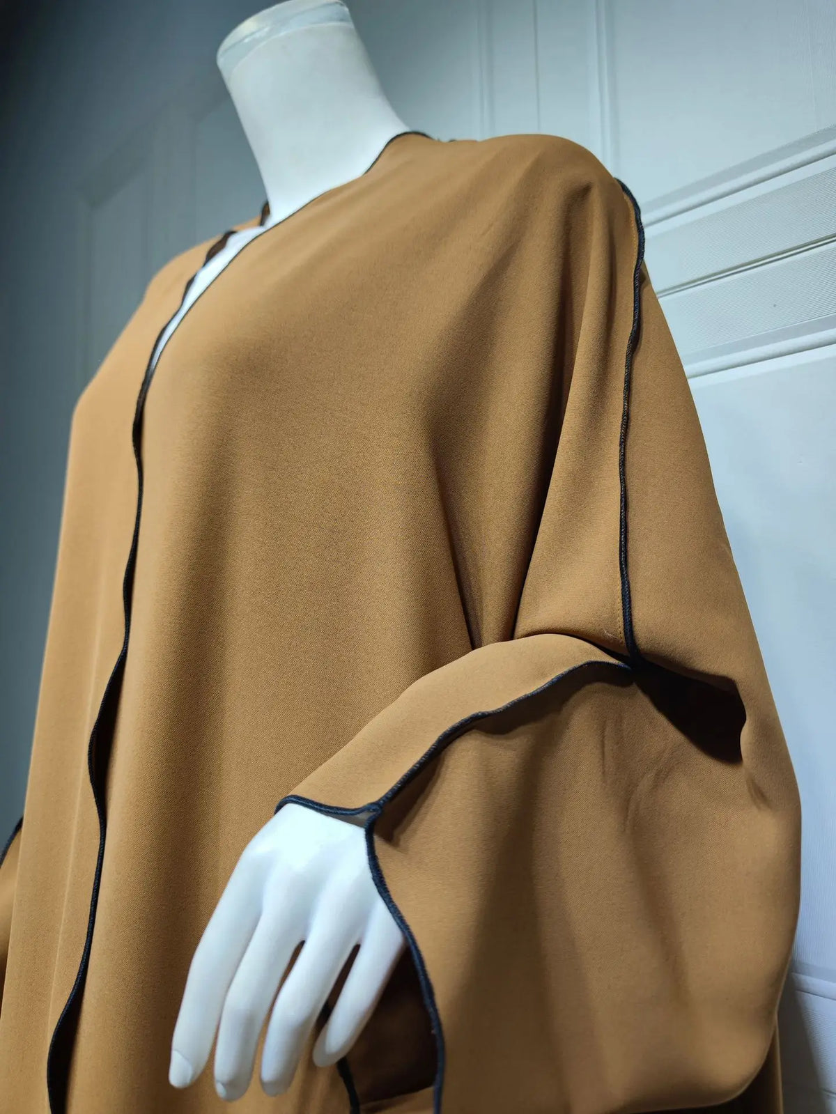 Una modelo viste una abaya marrón suelta y de largo completo con ribetes negros en un maniquí blanco.