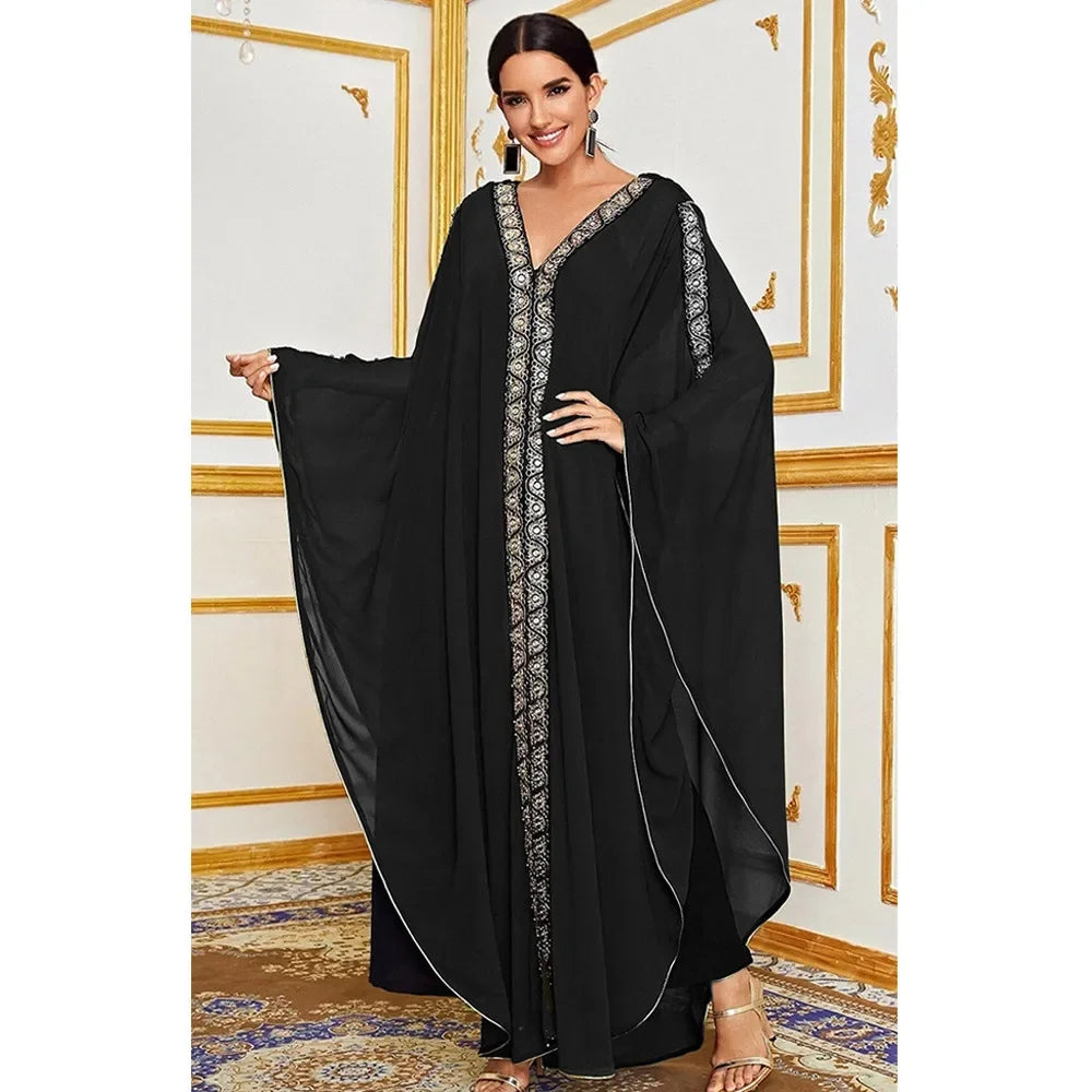 Una mujer modela un vestido maxi abaya negro y fluido con mangas de murciélago, bordado plateado y ribete dorado.