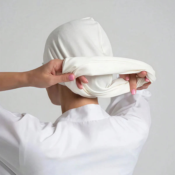 A person is adjusting a white premium stretch cotton instant hijab headscarf on their head.