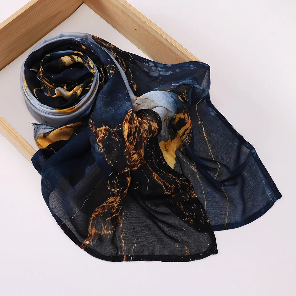 Voile hijab imprimé bleu foncé avec motifs abstraits or et brun, drapé sur un cadre en bois.