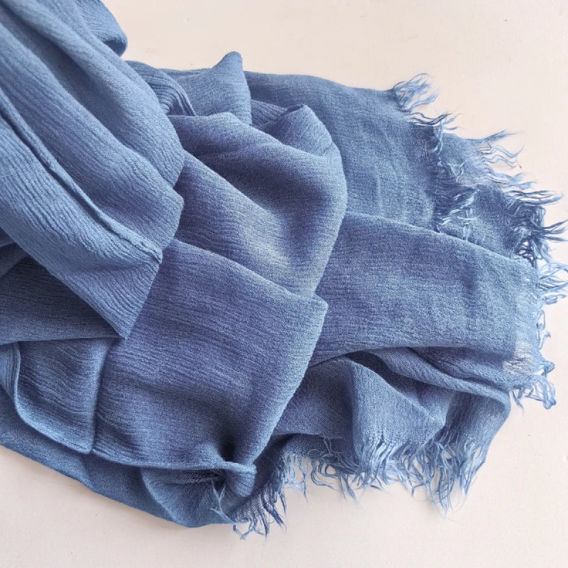 Un foulard hijab en coton viscose bleu doux avec pompons, drapé sur une surface blanche.