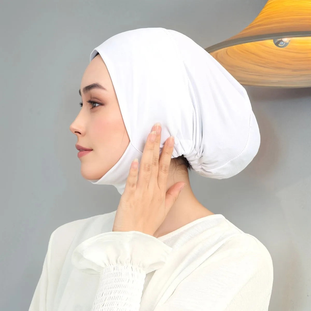 Une femme portant un foulard hijab blanc uni, regardant sur le côté et touchant ses cheveux.