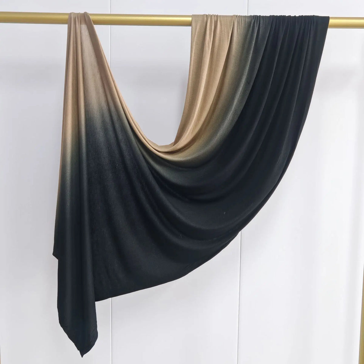 Pañuelo de algodón con degradado negro y bronce colgado en un palo de madera.