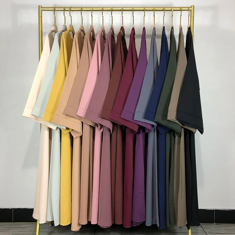 Exposition d'abayas de couleurs variées suspendues sur un présentoir doré.
