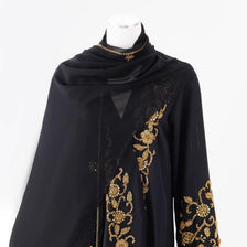 Abaya negra transparente con bordado floral dorado y detalles de cuentas, exhibida en maniquí.