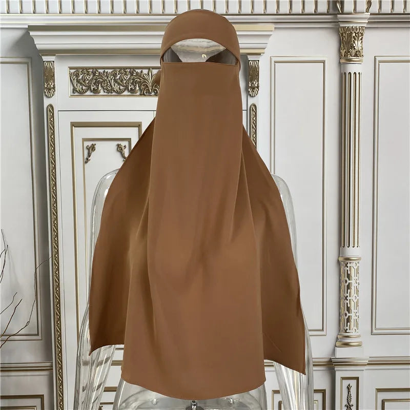 Eine braune elegante Maxi-Abaya auf einem Mannequin vor verzierten weißen architektonischen Zierleisten.