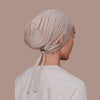 Une toque intérieure de hijab beige à cordon portée par une femme, vue de profil.