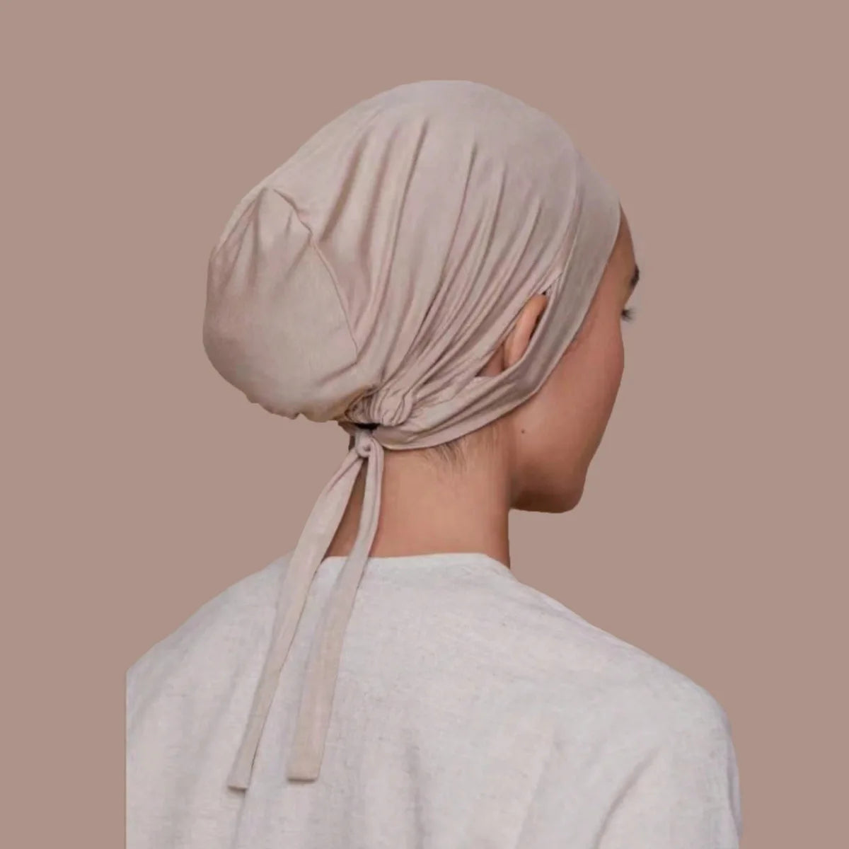 Une toque intérieure de hijab beige à cordon portée par une femme, vue de profil.