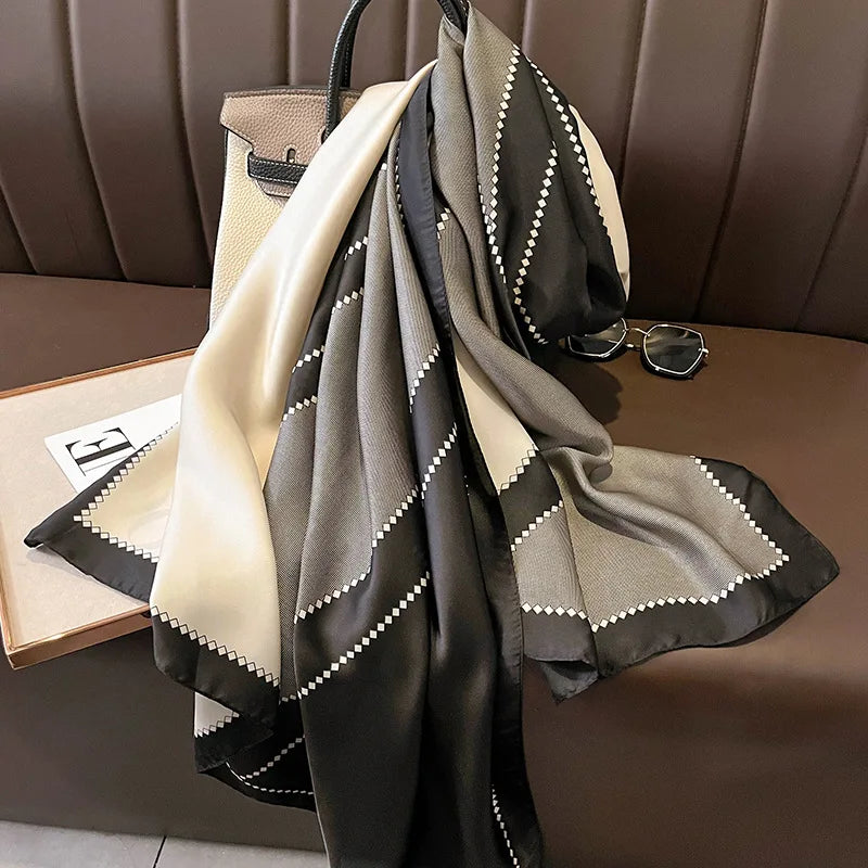 Ein drapierter Feder-Pareo-Schal aus Seide in Schwarz, Grau und Creme auf einer braunen Lederoberfläche.
