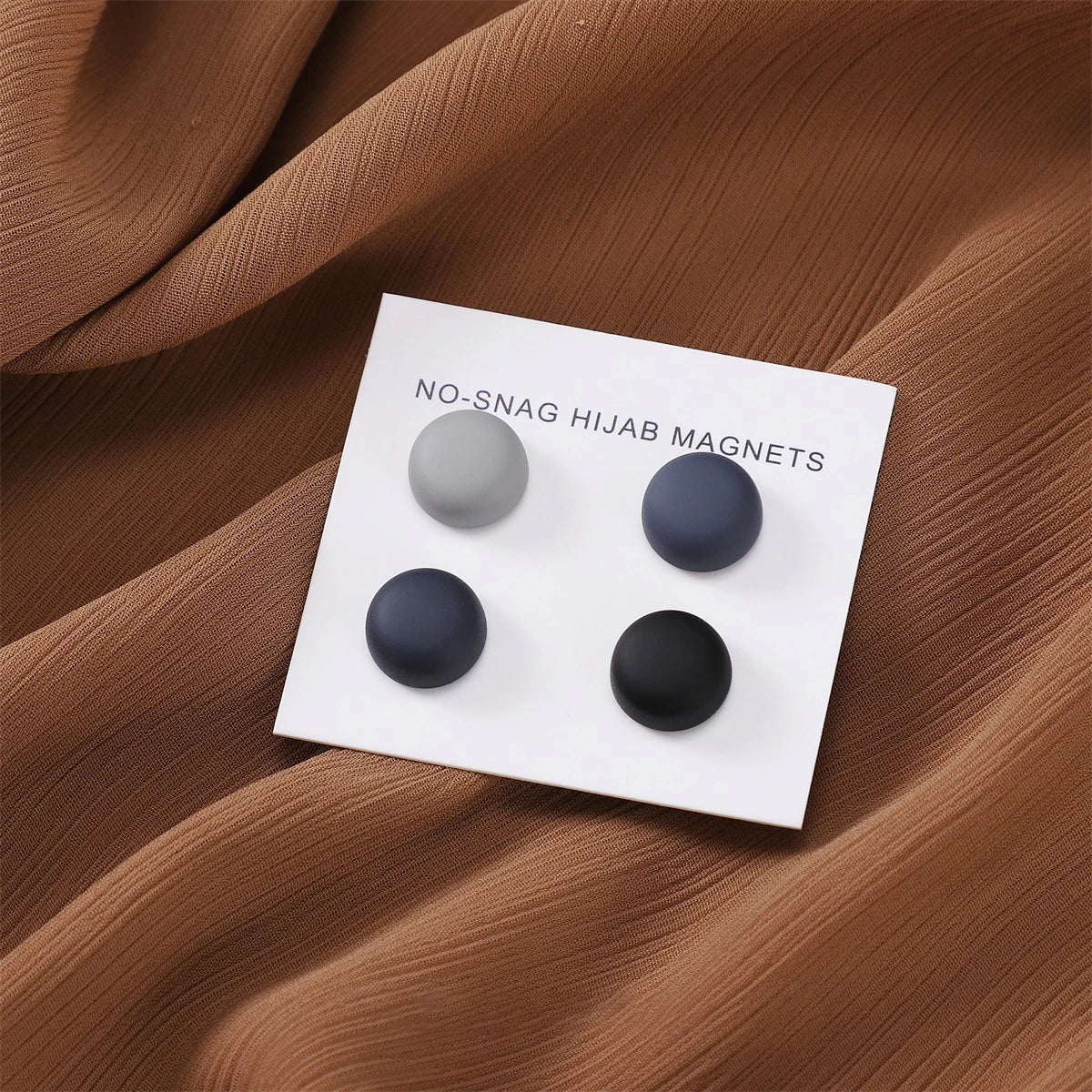 Weiße magnetische Hijab-Pins mit vier matten Magneten auf braunem Stoff.