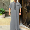 A man wearing a grey Moroccan ethnic thobe with a stand collar standing in a doorway.