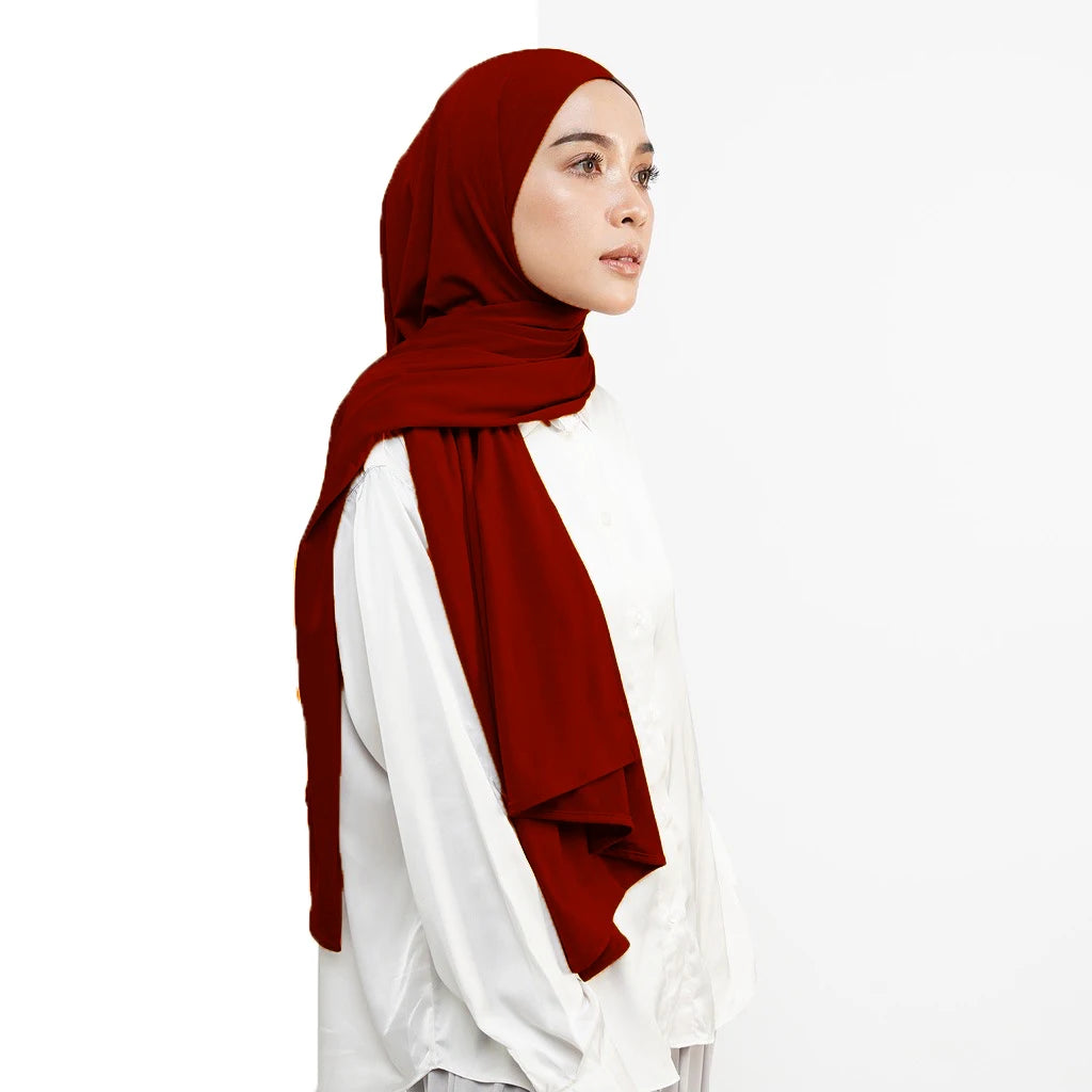 Eine Frau in rocher roter Hijab und weißer Kleidung, die zur Seite blickt.