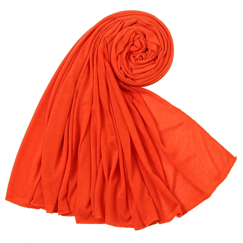 Un foulard hijab en jersey de coton orange vif, roulé en spirale et drapé, montrant sa texture douce.
